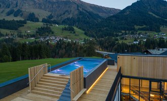 A modern terrace with a pool and wooden flooring, surrounded by picturesque mountains. The view of the landscape is stunning and conveys a sense of tranquility. | © Genuss- & Aktivhotel Sonnenburg |Heike Wohlgenannt