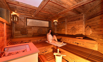 A cozy sauna with wooden walls and benches. A relaxed person is sitting in the room and enjoying the warmth.