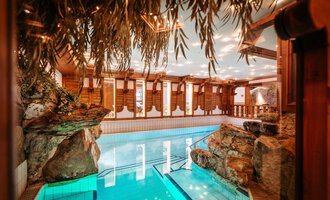 An elegant indoor pool with clear water and rocks in the background. The wooden paneling and soft lighting create a relaxed atmosphere.