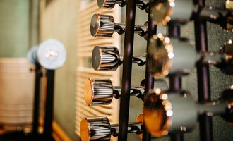 A series of dumbbells in a gym. The background is blurred and shows textures of the walls.