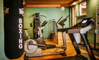 A modern gym with various training equipment. In the foreground, a treadmill and a punching bag are visible.