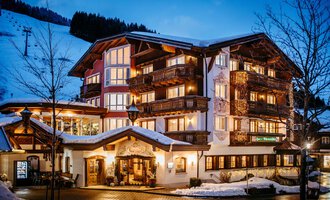 A cozy hotel in the mountains at night. The facade is illuminated and surrounded by snow-covered trees.