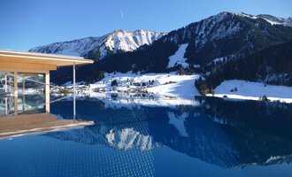 An infinity pool overlooking snow-capped mountains. The clear sky and calm water surface reflect the winter landscape. | © Hotel Erlebach | Kristin Winter