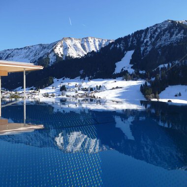 An infinity pool overlooking snow-capped mountains. The clear sky and calm water surface reflect the winter landscape. | © Hotel Erlebach | Kristin Winter