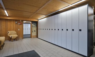 A modern changing room with white lockers against one wall. The room has a wooden ceiling and tiled floor. | © Sport Kessler GmbH