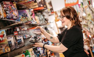 A woman is looking at a LEGO set in a toy store. She smiles and holds the packaging in her hand.