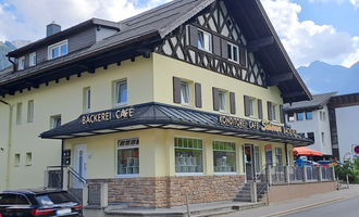 A nice café with a bakery in a traditional building. In the background, mountains and a blue sky are visible. | © Kleinwalsertal Tourismus | Steffen Stöhr
