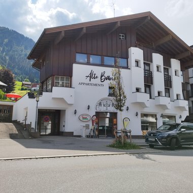 A modern building with a wooden and plaster facade that offers apartments. In the background, green mountains and a blue sky can be seen. | © Kleinwalsertal Tourismus | N. Lughammer