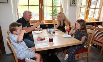 A family enjoys their food and ice cream in a cozy restaurant. They are laughing and having fun at the table. | © Familienhotel Kleinwalsertal Hotelgesellschaft mbH