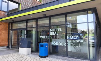 Ein modernes Schulgebäude mit großen Fenstern und einem einladenden Eingang. Die Fassade zeigt die Namen verschiedener Schularten. | © Kleinwalsertal Tourismus | Veronika Senn