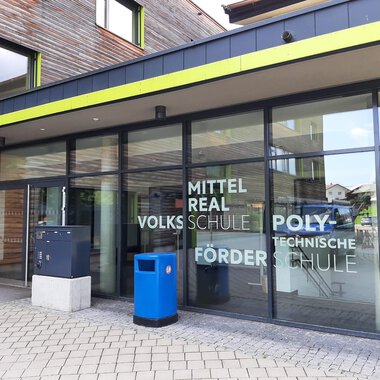 Ein modernes Schulgebäude mit großen Fenstern und einem einladenden Eingang. Die Fassade zeigt die Namen verschiedener Schularten. | © Kleinwalsertal Tourismus | Veronika Senn