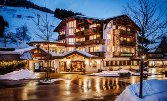 A charming hotel in winter with snow-covered mountains in the background. The warm lights of the house shine in the twilight.