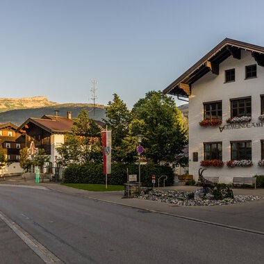 A picturesque street view of a small village in the Alps, surrounded by mountains. The charming houses are adorned with flowers, creating an inviting atmosphere. | © Kleinwalsertal Tourismus |  Steffen Berschin