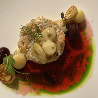 A beautifully arranged plate with a fish specialty, surrounded by various sauces and vegetables. The colors are vibrant and create an appealing visual impression.