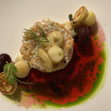 A beautifully arranged plate with a fish specialty, surrounded by various sauces and vegetables. The colors are vibrant and create an appealing visual impression.