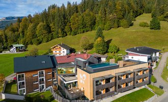 A modern hotel building in a picturesque landscape with green meadows and wooded hills. The surroundings are calm and inviting, ideal for those seeking relaxation.