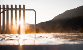 A relaxing thermal bath with a steaming water surface. In the background are gentle hills and a clear sky.