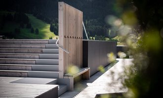 A modern terrace with a wooden structure and gentle steps. In the background, green hills and trees can be seen.