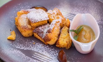 A plate with golden-brown, sugar-dusted pancake pieces and a bowl of applesauce. The dish looks appetizing and is garnished with fresh mint.