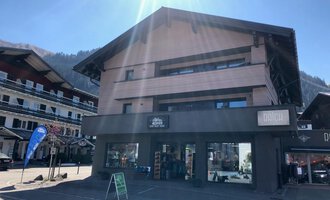 A modern building with several floors that has a commercial facade. It is located in a picturesque alpine village setting. | © Sport Hilbrand OG