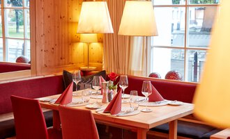 An inviting restaurant with wooden decor and a cozy atmosphere. The table is elegantly set and decorated with red napkins. | © Hotel Riezler Hof | M. Hasterok