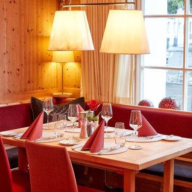 An inviting restaurant with wooden decor and a cozy atmosphere. The table is elegantly set and decorated with red napkins. | © Hotel Riezler Hof | M. Hasterok
