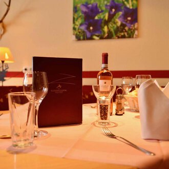 A beautifully set table in an elegant restaurant. On the table are glasses, a wine bottle, and a menu. | © IFA Breitach Apartements