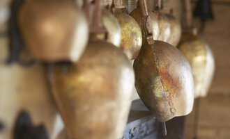 An ensemble of shiny golden bells hangs on a wall. The bells are of different sizes and share a rustic, handcrafted atmosphere.
