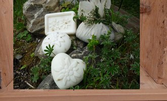 A bathroom with decorative soaps in heart and flower shapes. The soaps are placed on stones and green plant arrangements.