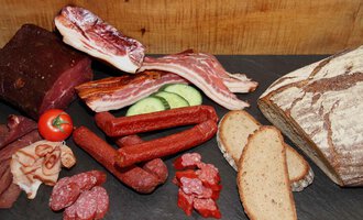 Eine Auswahl an Wurst und Fleisch auf einem schwarzen Untergrund, begleitet von scheiben Brot und frischem Gemüse. Die Anordnung ist appetitlich und rustikal. | © Innere Wiesalpe | Andrea Kainz zuckerschnecke.at