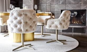 An elegant dining table with upholstered chairs in a light design. In the background, a fireplace can be seen, creating a cozy atmosphere. | © Travel Charme Ifen Hotel