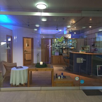 An inviting reception area with a bright, modern design. On the table, there is a candle and there are various products on the counter. | © Schönzeit | Sebastian Riezler