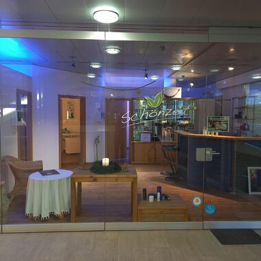 An inviting reception area with a bright, modern design. On the table, there is a candle and there are various products on the counter. | © Schönzeit | Sebastian Riezler