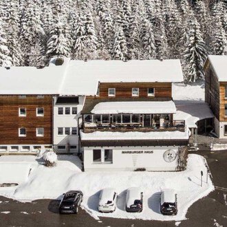 A snow-covered landscape with several buildings in chalet style. Surrounded by tall, snow-covered fir trees. | © Marburger Haus | Sweetchili
