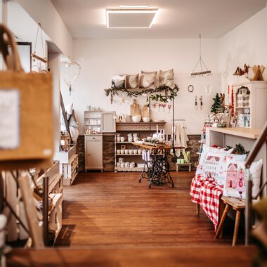 An inviting store with wooden flooring and stylish decorations.  
Shelves are filled with various products and cozy accessories.