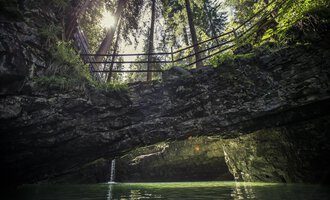 An idyllic place with clear waters and steep cliffs. In the background, tall trees and a sunbeam are visible. | © Kleinwalsertal Tourismus | Oliver Farys