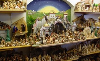 A detailed nativity scene with many figures and biblical scenes is arranged on shelves. In the background, a picturesque landscape with a sky can be seen. | © Nebelhorn Holzschnitzerei e.K.