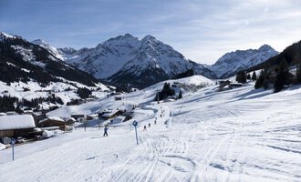 A snowy landscape with mountains in the background. Skiers enjoy the slopes in this peaceful winter scene. | © OBERSTDORF · KLEINWALSERTAL BERGBAHNEN