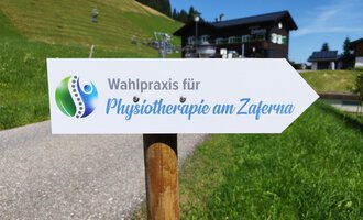 Ein Wegweiser zeigt zur Wahlpraxis für Physiotherapie am Zaferna. Die Umgebung ist grün und bergig, ideal für Erholung. | © Kleinwalsertal Tourismus | N. Lughammer