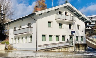 Ein modernes, dreistöckiges Gebäude mit weißen Wänden und grünen Fenstern. Es befindet sich in einer ruhigen Umgebung mit leichtem Schneefall. | © Polizeiinspektion Kleinwalsertal | C. Zwerger