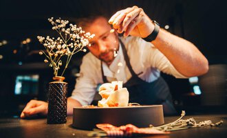 Our chief cook decorates a dish with a lot of love and skill. In the background, there is a small flower in a vase. | © Hotel Birkenhöhe | Stefan Klauser