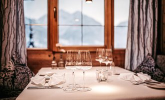 An elegantly set table with glasses and napkins. In the background, one can see a beautiful mountain landscape through the window.
