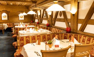 A cozy restaurant with wooden walls and elegant table decorations. Colorful tablecloths and warm lighting create an inviting atmosphere. | © Hotel Alte Krone