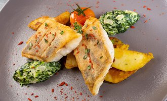 A plate with fried fish fillet, crispy potatoes, and steamed spinach. Fresh tomatoes and spices add an appealing look. | © Hotel Alte Krone