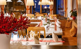 A cozy restaurant with elegantly set tables and warm light. Red accents from flowers and decorations create an inviting atmosphere. | © Hotel Alte Krone