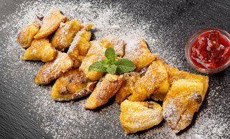 A delicious serving of baked dough pieces with powdered sugar and fresh mint. Served alongside is a glass of red jam. | © Hotel Alte Krone