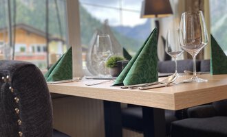 An elegant table with green napkins and glasses. In the background are mountains and windows that let in a lot of light. | © Robert Haller GmbH c/o Hotel Steinbock