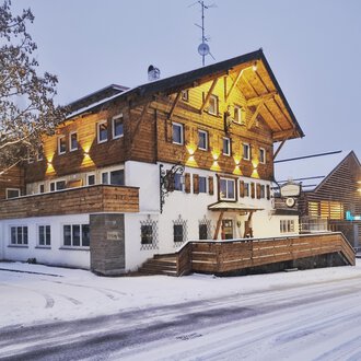 A charming wooden house in the snow, illuminated by warm light. The surroundings are wintry and inviting. | © Hotel Neue Krone GmbH | Werbewind GmbH