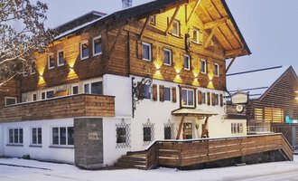 A charming wooden house in the snow, illuminated by warm light. The surroundings are wintry and inviting. | © Hotel Neue Krone GmbH | Werbewind GmbH