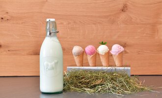 A bottle of milk stands next to waffles with different ice cream flavors. The waffles are colorful and presented on a rustic background. | © Hotel Neue Krone GmbH | Werbewind GmbH